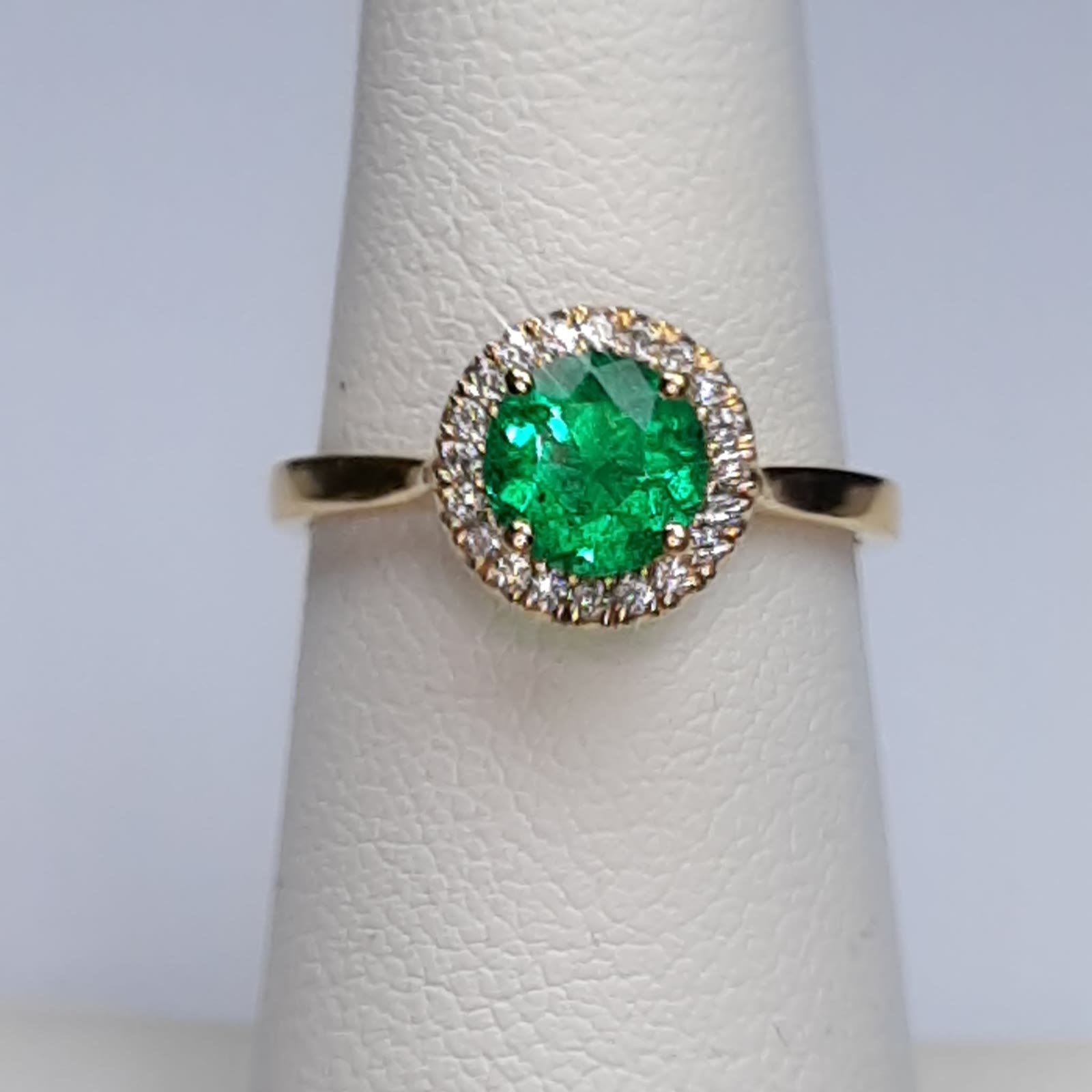 Round-cut Colombian emerald ring surrounded by 20 natural diamonds in an 18K yellow gold halo setting.